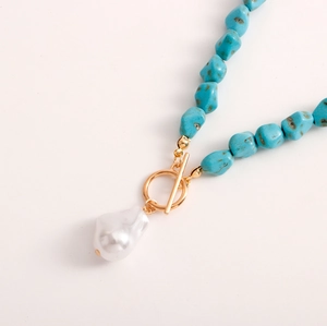 Detailed macro view of irregular blue turquoise beads and baroque pearl pendant on gold necklace