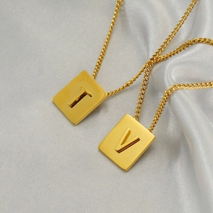 Gold rectangular pendant necklaces with letters T and V on white silk background