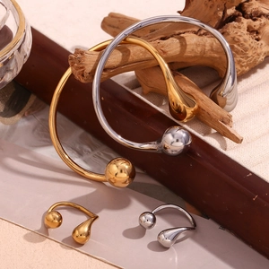 Polished double teardrop open bangles and rings in gold and silver finish on wood