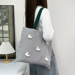Detail of striped canvas tote bag featuring cute duck plush charms and green strap