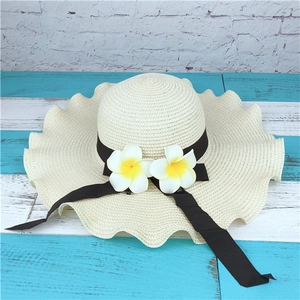 Close-up of cream straw hat with wavy brim, black ribbon, and tropical frangipani flowers