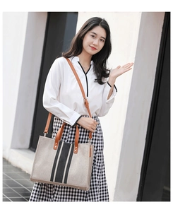 Detail of canvas tote bag featuring vertical stripes and brown leather handles in outdoor setting