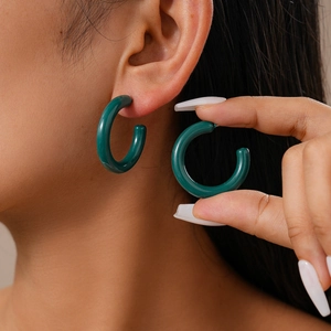 Detail of dark green chunky acrylic C-shaped hoop earring worn for size reference