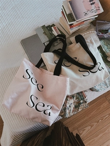 Flat lay of pink and beige canvas tote bags with See Sea print and black handles