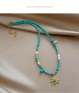 Détail du collier de perles turquoise avec pendentif soleil doré sur satin de soie