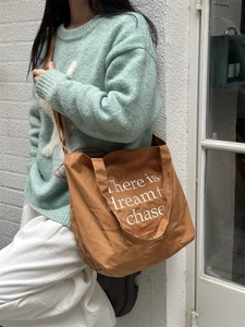 Brown canvas tote bag with dream quote print shown on a side-wearing model