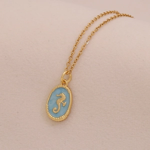 Macro shot of gold seahorse pendant with blue enamel inlay and textured metal edge