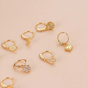 Golden nose rings with zircon cross and evil eye charms on light beige background