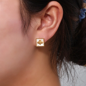 Macro shot of square gold bee stud earrings with white inlay and beaded edge on ear