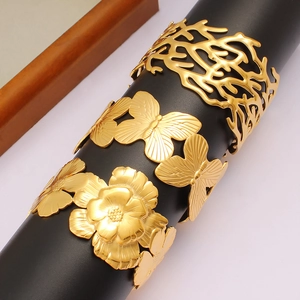 Three gold cutout stainless steel bangles with floral and butterfly patterns on stand