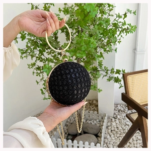 Spherical black evening bag with gold ring handle and sequins shown in a garden setting