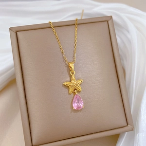 Titanium gold starfish necklace featuring a pink teardrop gemstone on a jewelry cushion