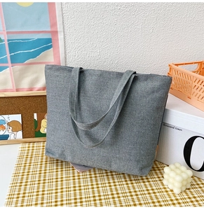 Minimalist grey canvas tote bag displayed on a checkered tablecloth with lifestyle decor