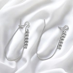 Silver stainless steel heart earrings with small crystals on white silk fabric background