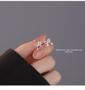 Macro detail of S999 silver bow earrings held by hand on a minimalist dark background