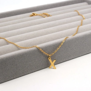 Close-up of golden letter X pendant on stainless steel chain over velvet display