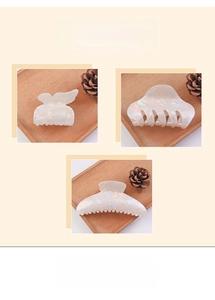 Three elegant pearl white iridescent hair claws displayed on wooden trays with pine cones