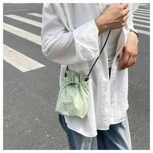 Street style shot of light green bucket bag with drawstring and black crossbody strap