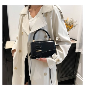 Detail of a chic black leather handbag with gold metal clasp and handle on white coat