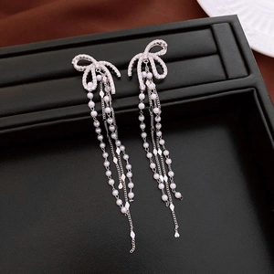 Macro detail of silver bow earrings with zircon pavé and hanging pearl tassels