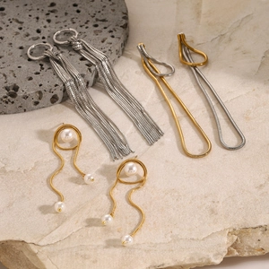 Set of stainless steel tassel, two-tone snake chain, and pearl accent earrings on stone
