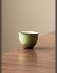 Detail of a kiln-fired ceramic tea cup with yellow-green glaze and speckled texture