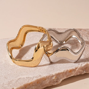 Irregular wavy metal bangles in gold and silver finish on natural stone background