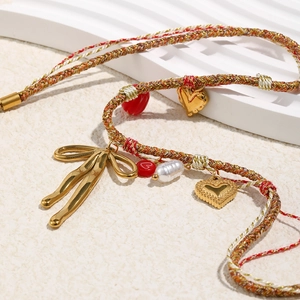 Detail of woven necklace with butterfly and heart charms on a sand texture background