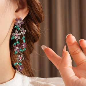 Gros plan de longues boucles d'oreilles fleurs vintage avec strass violets et verts sur modèle
