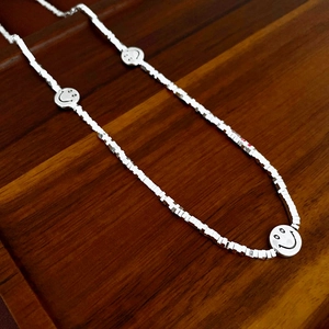 Detail of silver smiley face necklace with three pendants on a wood tray
