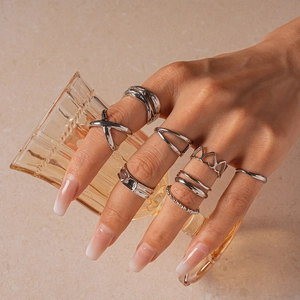 Close-up of seven silver geometric rings on a hand holding a transparent cup