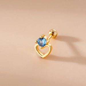 Macro detail of golden hollow heart stud earring with a round blue gemstone inlay