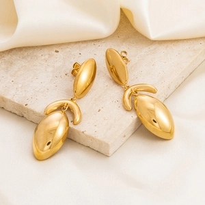 Close-up of gold leaf-shaped dangle earrings on beige slate and cream silk fabric