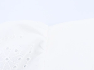Gros plan sur une blouse blanche française montrant les détails de broderie ajourée