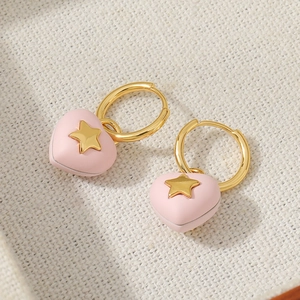 Pink heart drop earrings with gold stars and brass hoops on a woven background