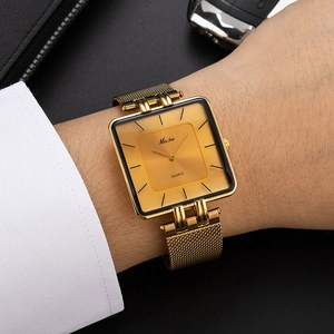 Elegant gold square quartz watch with Milanese mesh strap on wrist against dark background