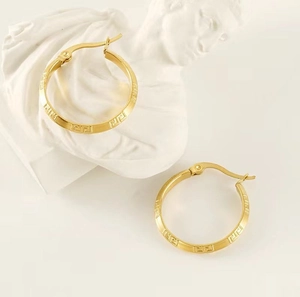 Detail of 18K gold stainless steel hoop earrings with Greek key pattern on white marble