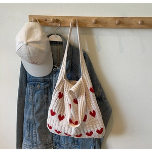 Detalle de bolso de punto beige con corazones colgado en gancho con chaqueta vaquera