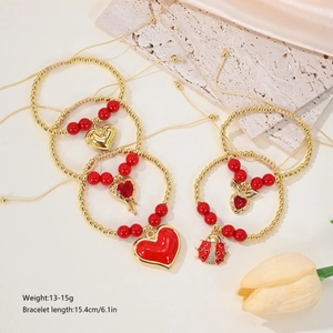 Detail of 18k gold plated beaded bracelets with heart and ladybug charms on silk background
