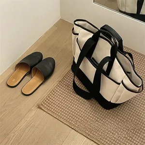 Detail of a large black and white canvas tote bag next to black loafers on a woven mat
