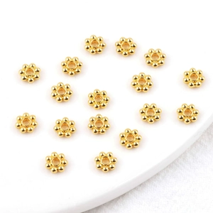 Multiple 14k gold plated flower spacer beads for DIY jewelry making on white ceramic