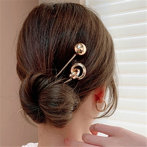 Close-up of a sleek golden geometric metal hair stick styled in a woman's elegant bun