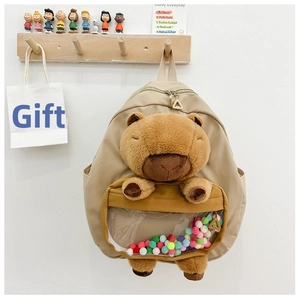 Detail of canvas backpack featuring a plush capybara and colorful pom-poms in a clear pocket