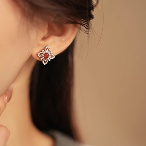 Close-up of a silver flower earring with a red gemstone on a model's ear lobe