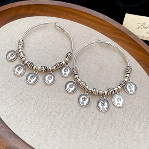 Detailed macro of vintage silver hoops with Elizabeth coin pendants on linen