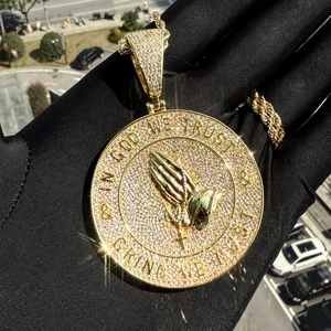 Close-up of golden hip hop pendant with praying hands and In God We Trust engraving
