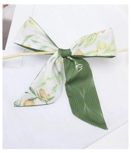 Detail of silk hair ribbon with green leaf and lemon print tied in a bow on a wooden rod