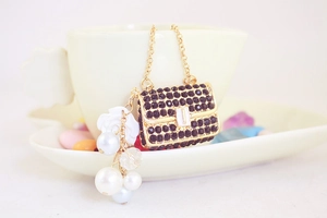 Detailed close-up of a golden mini handbag charm with black rhinestones and pearl tassel