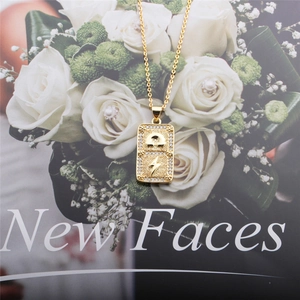 Detail of gold square necklace with lightning charm on magazine and white roses