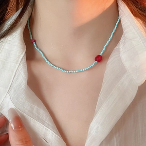Detail of beaded necklace with light blue and red beads on a white shirt background